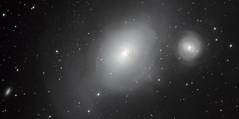 Two large white diffusive areas, galaxies with faint spiral structure, on black background with stars and smaller galaxies